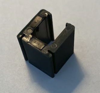Peça de conector de plástico preto em fundo claro.